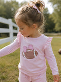 Little girl in a pink long-sleeve shirt with a football and bow design, playing outdoors.