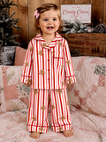 Smiling child in red and white striped pajamas with gingerbread, standing on a quilted bed.