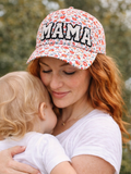 Mother cradles her child, wearing a floral cap with "MAMA" on it, in a soft, nature-filled background.