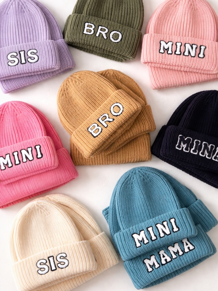 Colorful knit beanies with words "SIS," "BRO," "MINI," and "MAMA" displayed in various arrangements.