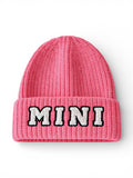 Pink knitted beanie with the word "MINI" embroidered in black and white on the front.