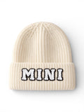 Cream-colored knit beanie with "MINI" embroidered in black and white letters.