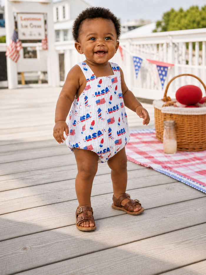 Smiling toddler in a NASA-themed outfit stands on wooden deck, surrounded by picnic setup and decorations.