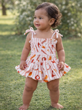 Smiling toddler wearing a floral-patterned dress, standing on grass in a sunny outdoor setting.
