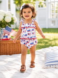 Smiling toddler in red, white, and blue outfit, walking on grass near decorations and flowers.