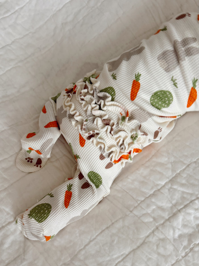 Baby outfit with a carrot and cactus print on a textured white background, featuring ruffled detailing.