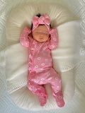 Baby girl in pink floral pajamas and bow, peacefully sleeping on a soft, white pillow.