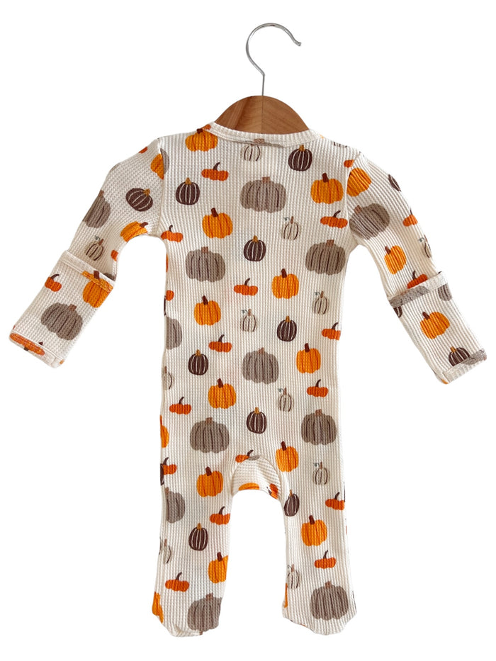 Infant onesie with a pumpkin print in orange and brown shades, hanging on a wooden hanger.