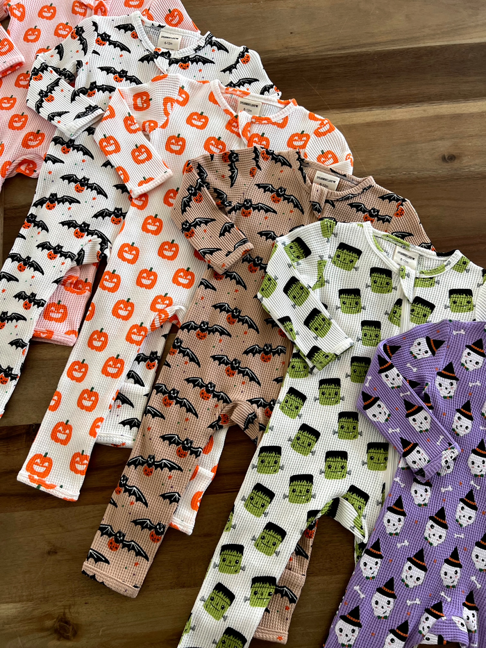 Assorted Halloween-themed baby pajamas in various colors and patterns on a wooden surface.
