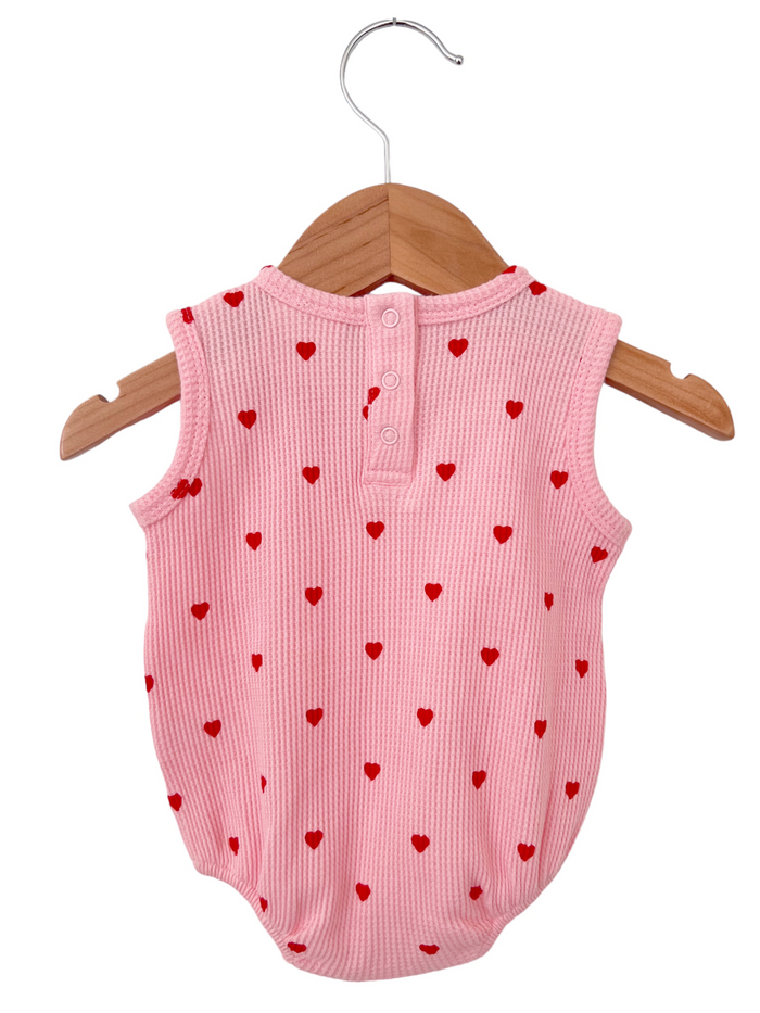 Pink baby romper with red heart patterns, displayed on a wooden hanger against a white background.
