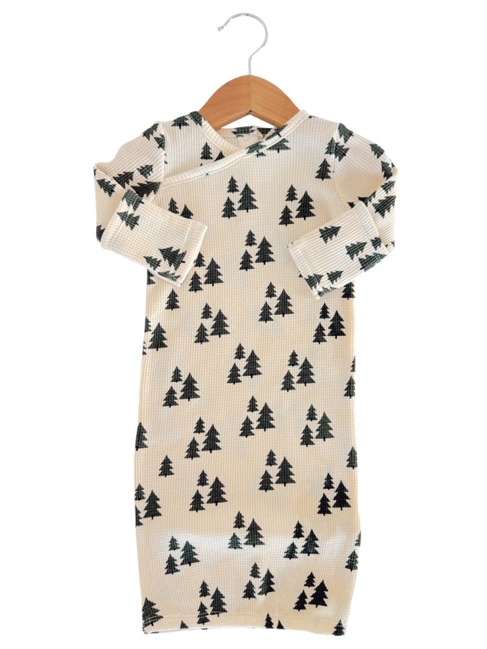 Infant outfit featuring a cream fabric with green tree patterns, displayed on a wooden hanger.