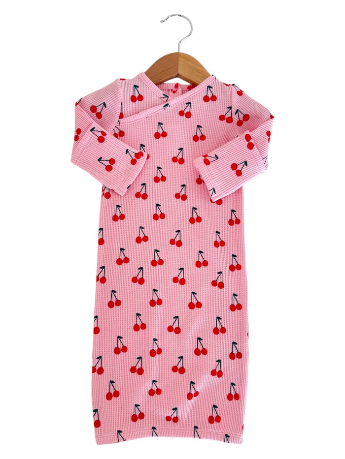 Pink children's dress with cherry print, featuring long sleeves and a hanging loop. Suitable for casual wear.