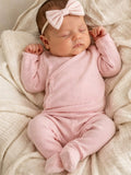 Sleeping baby girl in a pink outfit with a bow, nestled on a soft, textured blanket.