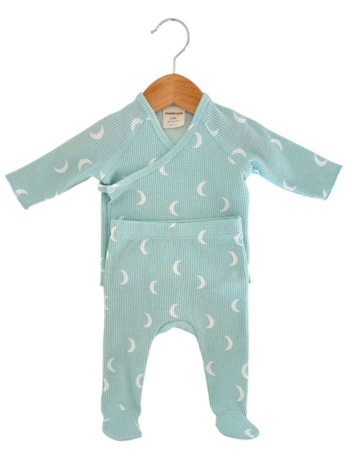 Light blue baby outfit with crescent moon pattern, hung on a wooden hanger.