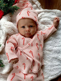 Baby in candy cane pajamas lying on a white blanket, surrounded by festive greenery.