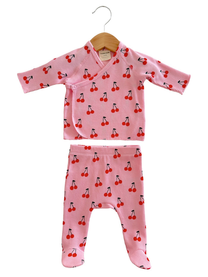 Baby outfit featuring a pink top and pants, both adorned with a cherry pattern. Ideal for comfortable wear.