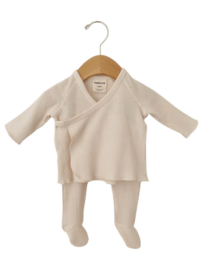 Cream-colored infant outfit with long sleeves and pants, displayed on a wooden hanger.