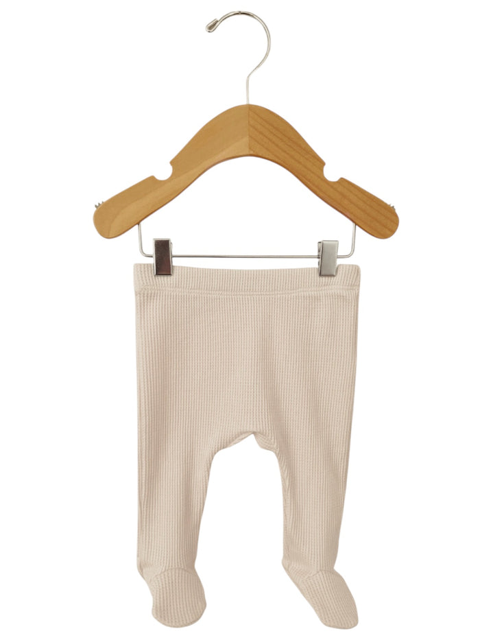 Pale beige baby leggings hanging on a wooden hanger against a white background.