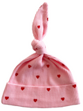 Pink knit baby hat with red heart patterns and a knot on top.