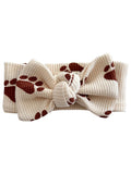 Cream headband with a large bow, featuring brown paw print patterns, ideal for pet lovers.