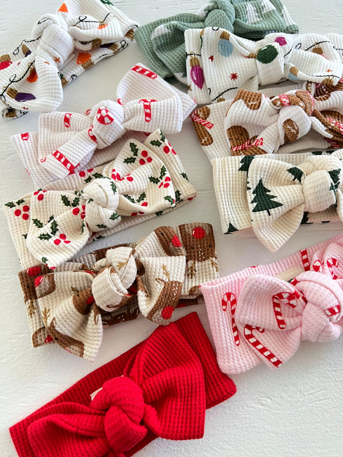 A collection of colorful fabric headbands with festive holiday patterns and bows arranged on a light background.