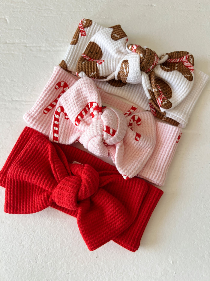 Three festive headbands: red, pink with candy canes, and white with gingerbread cookies. Perfect for holiday styling.