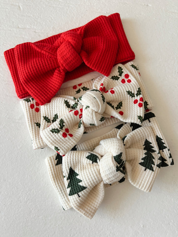Three festive headbands: a red one, and two patterned with holly and Christmas trees. Perfect for holiday styling.