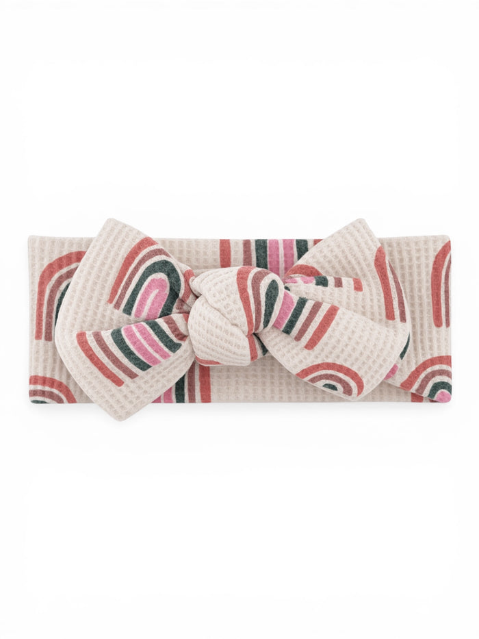 Beige headband with colorful rainbow patterns and a large bow at the center.
