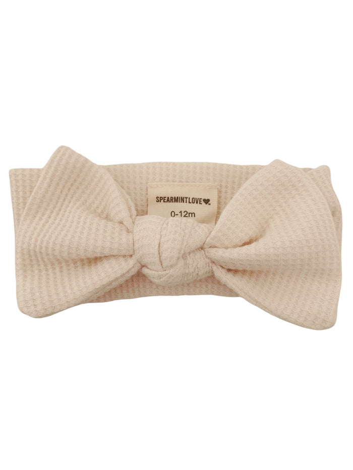 Beige baby headband with a large bow designed for ages 0-12 months, featuring a textured fabric.