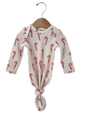 White baby onesie with red candy cane print, knotted at the bottom, hanging on a wooden hanger.