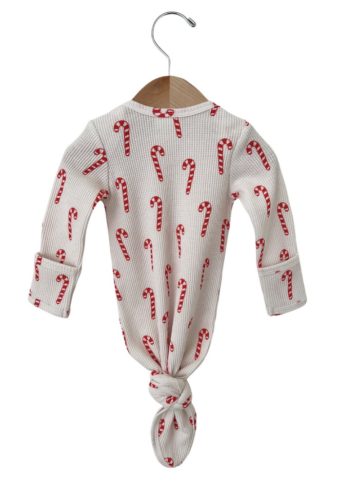White long-sleeve onesie with red candy cane pattern, tied at the bottom, hanging on a wooden hanger.