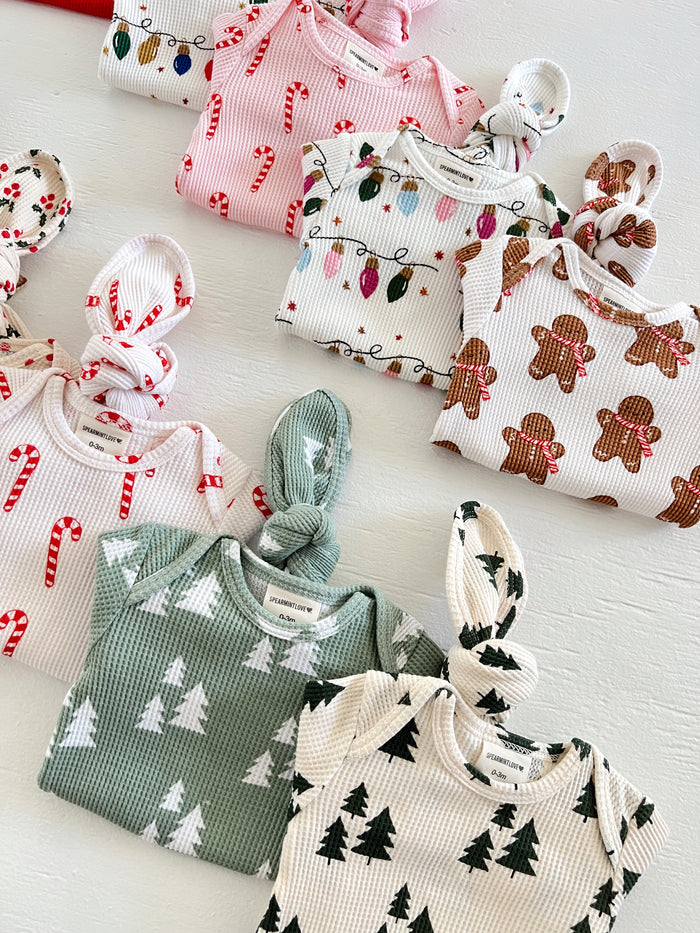 Colorful baby outfits with festive patterns including candy canes, Christmas lights, gingerbread, and trees.