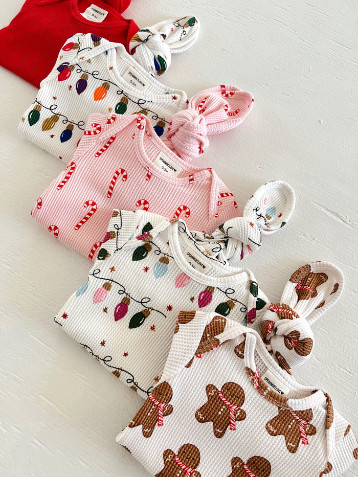 Colorful baby clothes in holiday patterns, including candy canes, lights, and gingerbread, laid out on a white surface.