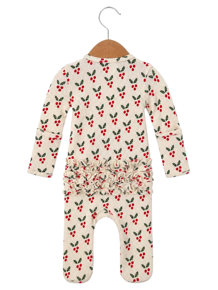 White romper with red berry and green leaf print, featuring a ruffled waist, hanging on a wooden hanger.