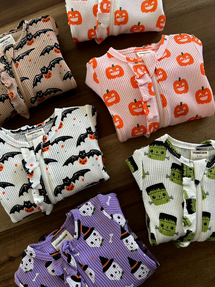 Colorful Halloween-themed baby pajamas featuring bats, pumpkins, ghosts, and Frankenstein designs.