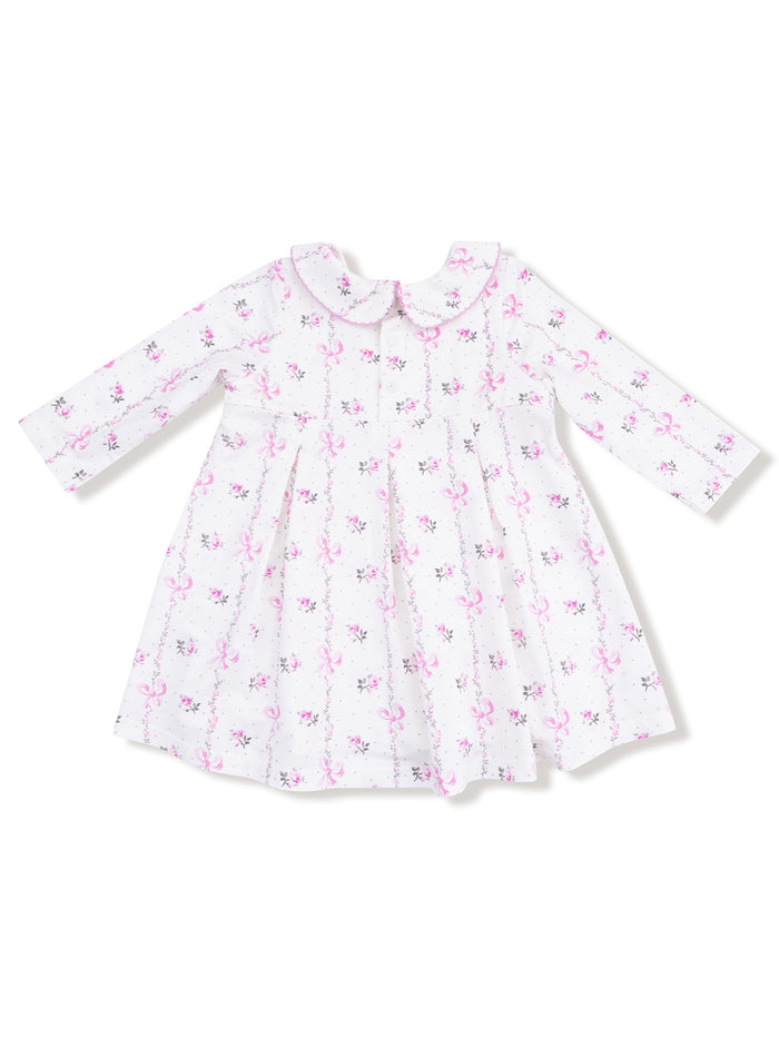 White dress with pink floral and bow print, featuring long sleeves and a rounded collar.