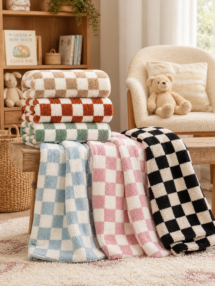 Stack of four colorful checkered towels and two draped towels on a wooden table in a cozy room setting.