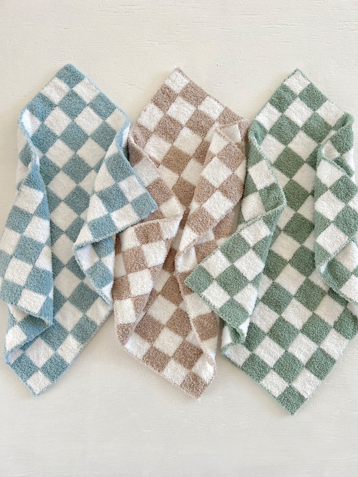 Three checkered towels in blue, brown, and green arranged on a light background.