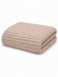 Beige waffle-patterned blanket folded neatly on a white background. Soft and cozy texture.