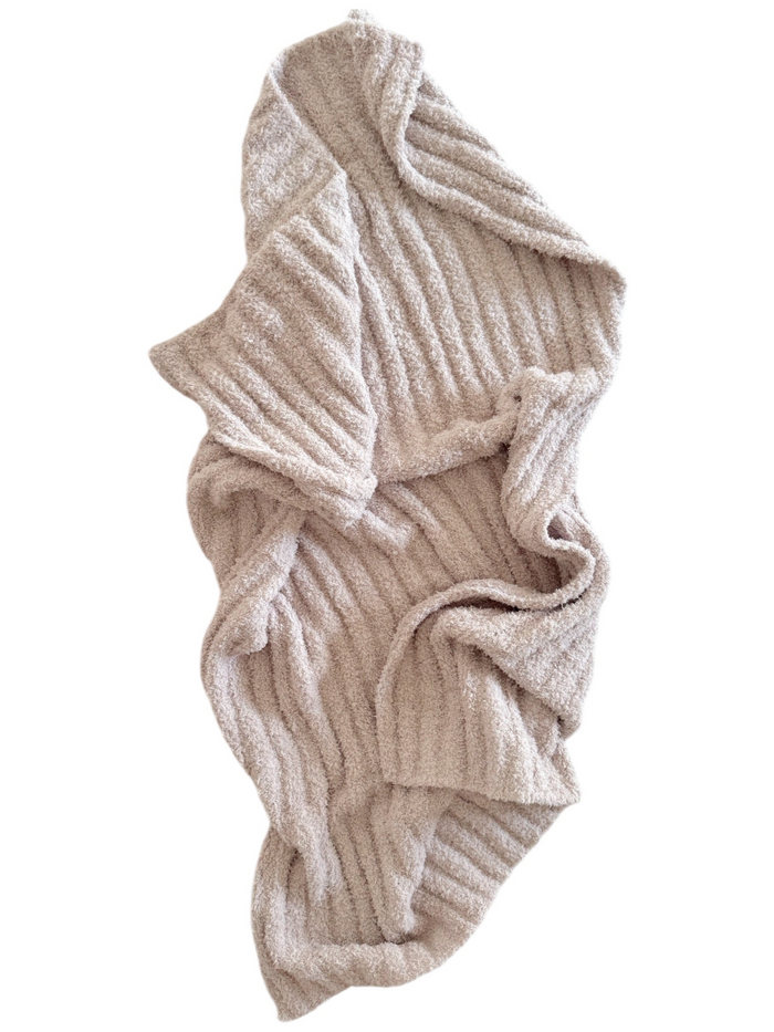 A folded, beige, textured blanket with a ribbed pattern laid out on a white background.