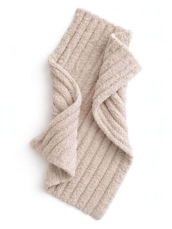 Beige ribbed scarf laid flat, showcasing its soft texture and folded design against a white background.