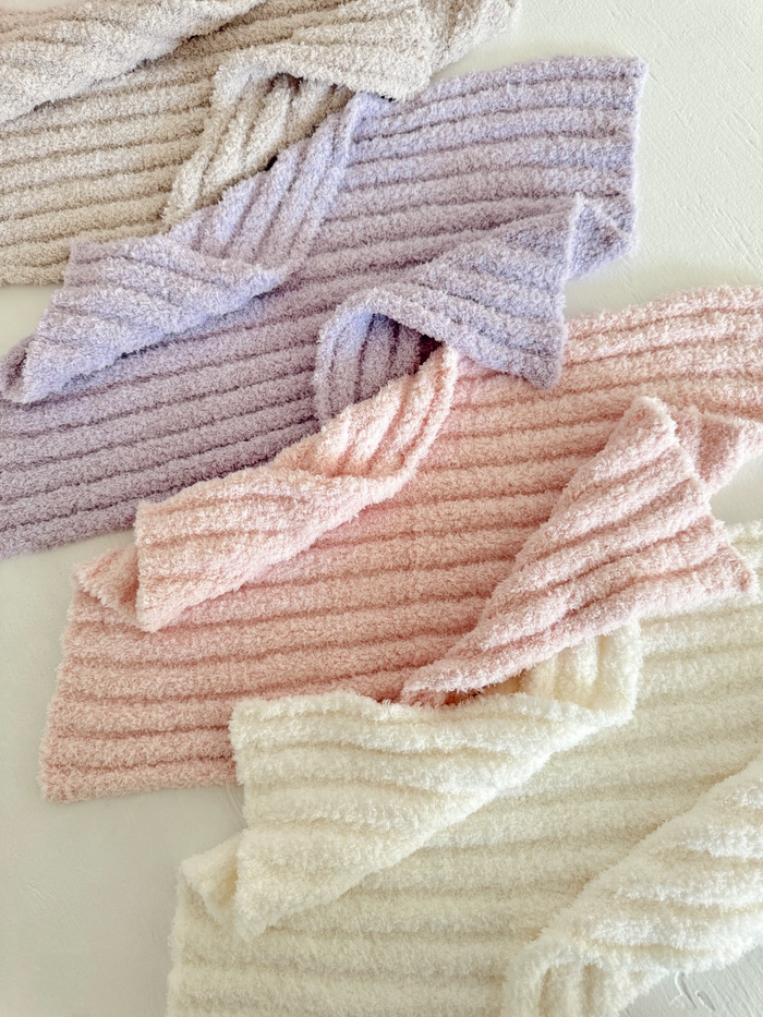 Soft, textured towels in pastel colors: pink, lavender, cream, and beige arranged stylishly on a light background.