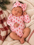 Sleeping baby in candy cane onesie with a matching headband, nestled on cozy blankets and greenery.