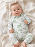 Smiling baby in green-patterned outfit on a cozy blanket, surrounded by a golf ball and soft textures.
