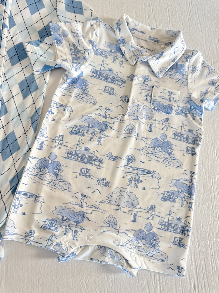 Blue and white children's romper with playful outdoor scenes, beside a blue plaid shirt.