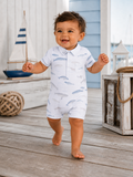 Smiling toddler in a whale-patterned outfit walking on wooden deck with nautical decor in the background.