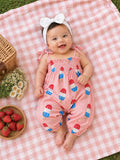 Smiling baby on a picnic blanket, wearing a pink outfit with popsicle prints, surrounded by strawberries and flowers.