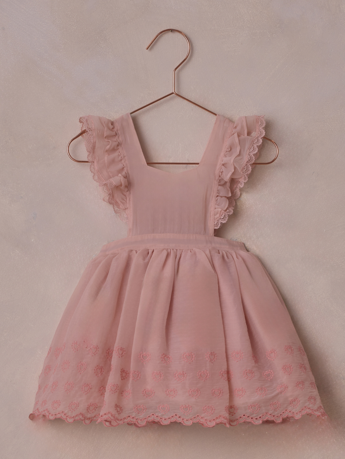 Pink dress with ruffled sleeves and heart embroidery, hanging on a copper hanger against a soft background.