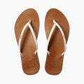A pair of Reef Cushion Slim Flip Flops with white straps and gold embroidery on a brown vegan leather base.