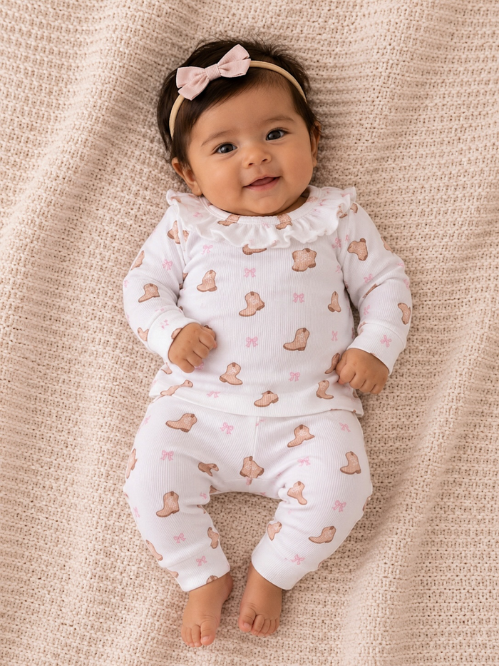 Smiling baby in a cozy outfit with a bear pattern and a pink bow headband, posed on a textured blanket.